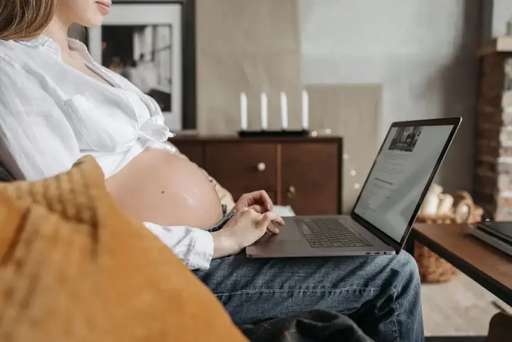 Kobieta w ciąży przy laptopie w salonie