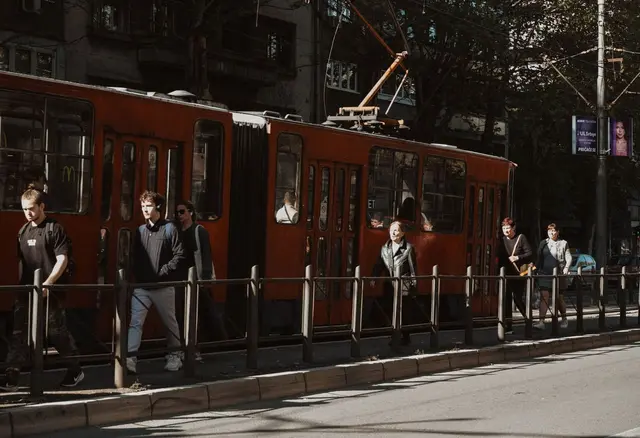 Ludzie idą obok czerwonego tramwaju