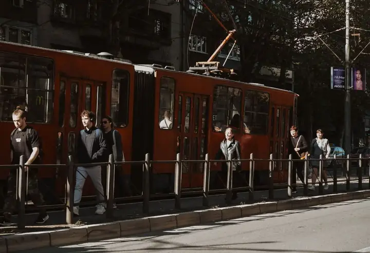 Ludzie idą obok czerwonego tramwaju