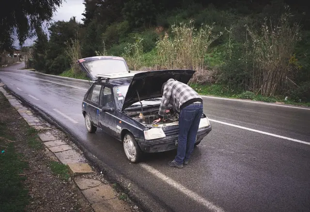 Mężczyzna naprawia zepsuty samochód na poboczu mokrej drogi