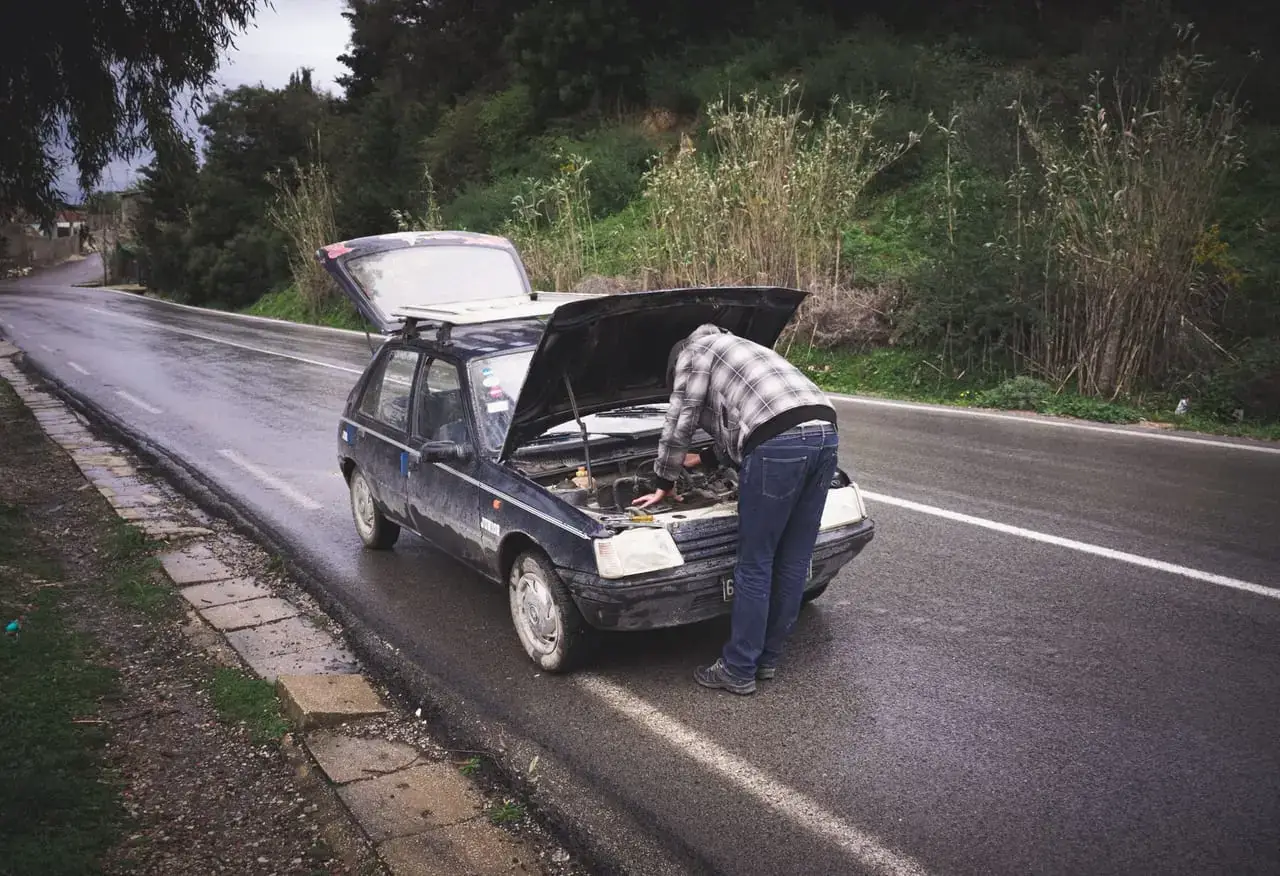 Mężczyzna naprawia zepsuty samochód na poboczu mokrej drogi
