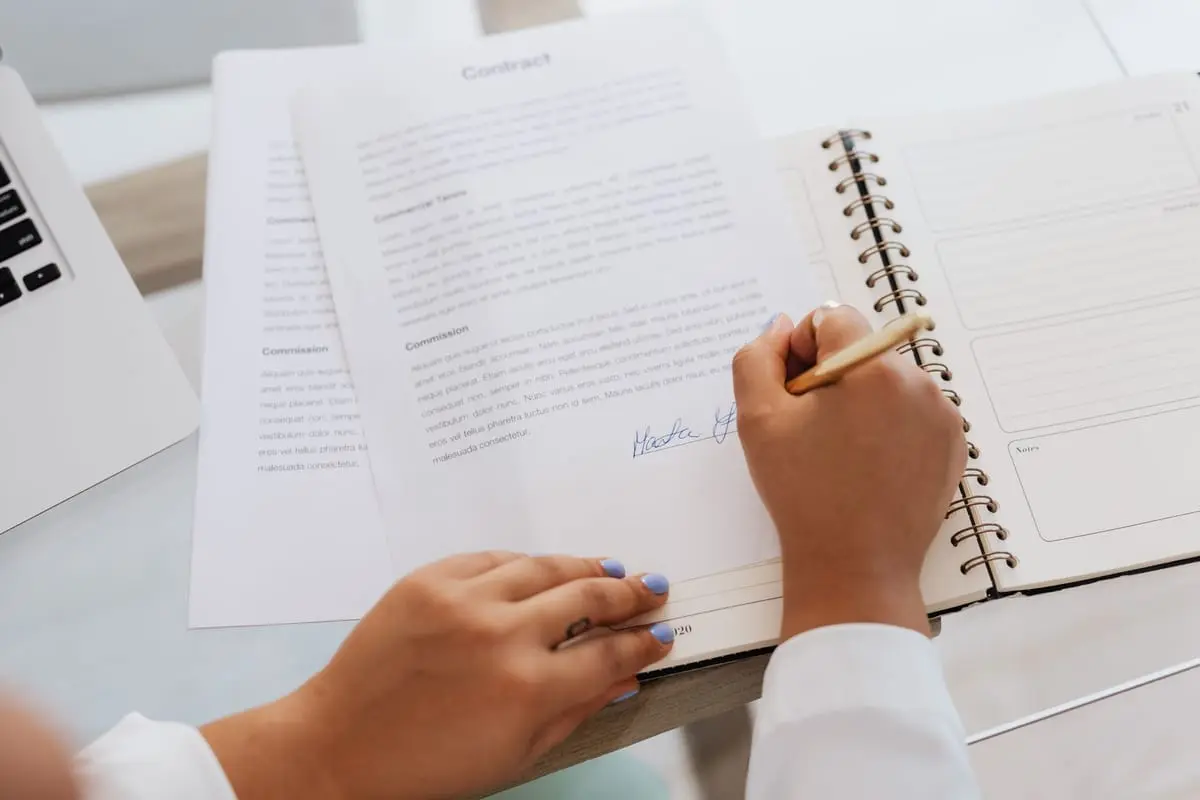 Dłonie podpisują dokument w notesie przy laptopie